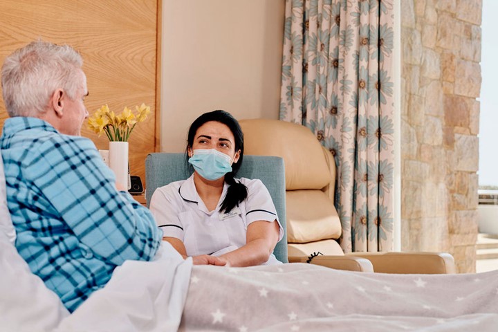 Image of patient in bed with nurse sat in chair next to him