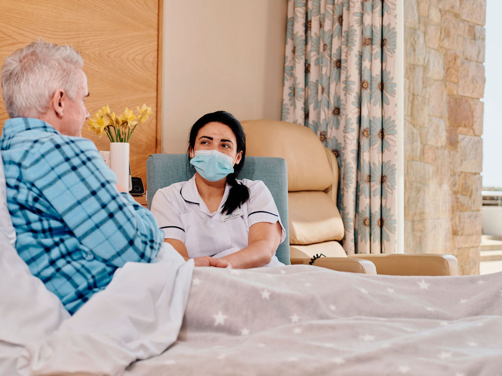 Image of patient in bed with nurse sat in chair next to him