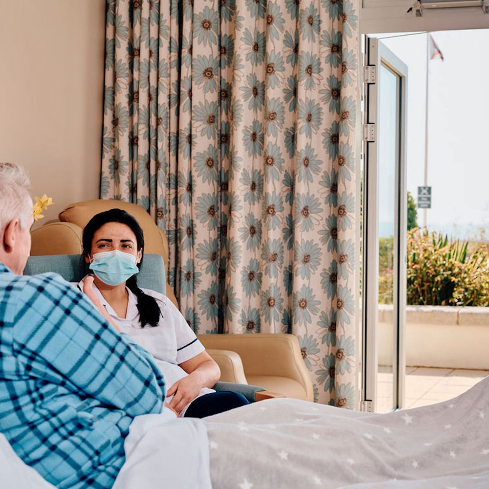 Image of patient in bed and nurse sat next to him 