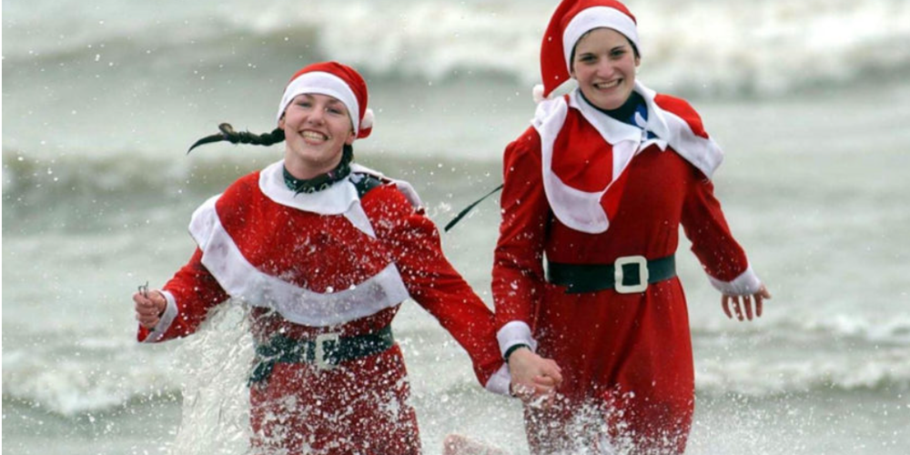 Image of two women in Santa suits running in the sea