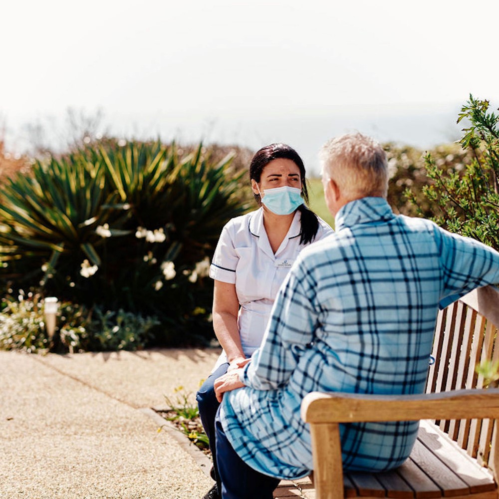 Image of nurse and patient sat on bench in gardens at Jersey Hospice Care