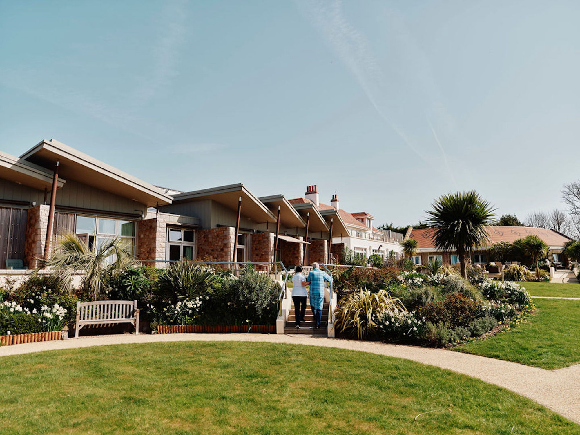 Image of nurse and patient walking up stairs in Hospice gardens with Hospice building behind them